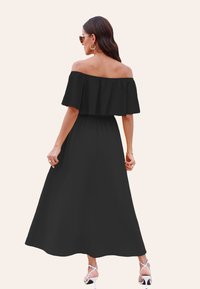 Abito maxi nero off-the-shoulder con cintura elastica, texture liscia e gonna fluente, abbinato a sandali bianchi con cinturini.