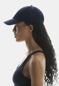 Navy blue baseball cap with a curved brim, made of soft fabric, features a side logo and is worn with a dark tank top.