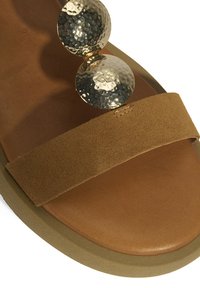 Tan suède instapsandalen met een brede band en een gouden gehamerde schijfaccent bovenop. Afgeronde zool met een glanzende afwerking aan de onderkant.