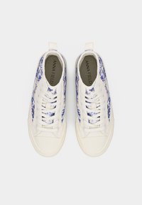 Λευκά πάνινα παπούτσια με μπλε λουλουδάτο σχέδιο, κορδόνια, θηλιές και το κείμενο "ANNA FIELD" στις εσωτερικές σόλες, σε θέα από πάνω σε λευκό φόντο.