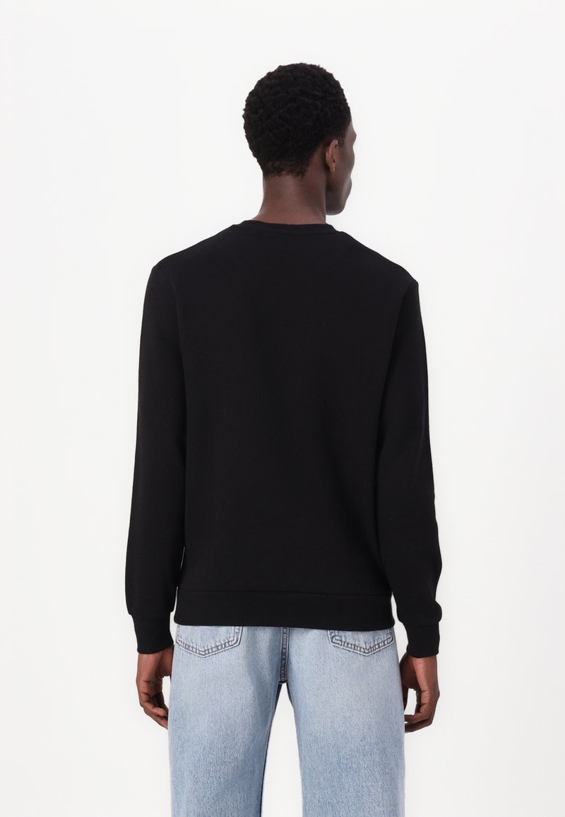 Schwarzer Sweatshirt mit langen Ärmeln, Rundhalsausschnitt und gerippten Bündchen. Getragen mit hellblauen Jeans, mit subtiler Textur im Stoff.