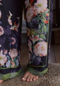 Pantaloni con motivo floreale caratterizzati da uno sfondo scuro, fioriture vivaci in toni di rosa, verde e viola, con un bordo verde sull'orlo.