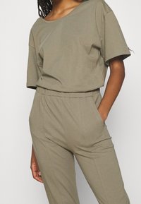 Conjunto de dos piezas color caqui hecho de una tela suave, que presenta una blusa corta y suelta con mangas cortas y pantalones con cintura elástica y bolsillos laterales.