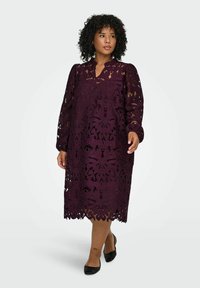 Duga rukava, tamnoljubičasta čipkasta haljina s cvjetnim izrezanim uzorcima, slojevitim dizajnom i zakrivljenim rubom, u kombinaciji s crnim cipelama.