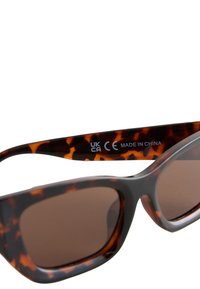 Braune Sonnenbrille mit Gestell aus Schildpatt-Acetat. Eckige Form mit getönten Gläsern, am Bügel sind die Aufschriften "MADE IN CHINA" und Zertifizierungslabels angebracht.