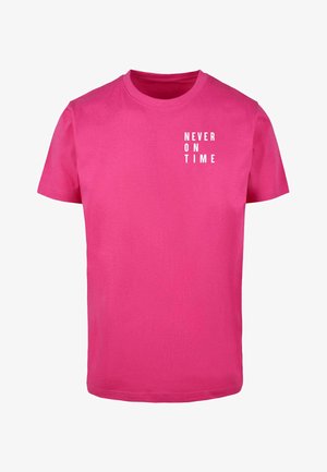 Rózsaszín pamut póló rövid ujjal és kerek nyakkal, az elülső részén fehér "SOHA NEM IDŐBEN" felirattal.