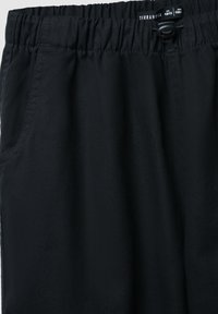 Pantaloni neri realizzati in tessuto morbido, con vita elastica dotata di cordino e tasche laterali. Senza motivi o accessori particolari.