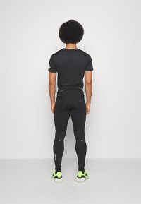 Maglietta sportiva nera e leggings attillati, con dettagli riflettenti. Le scarpe sono di un verde brillante con dettagli neri. Tessuto liscio e elasticizzato.