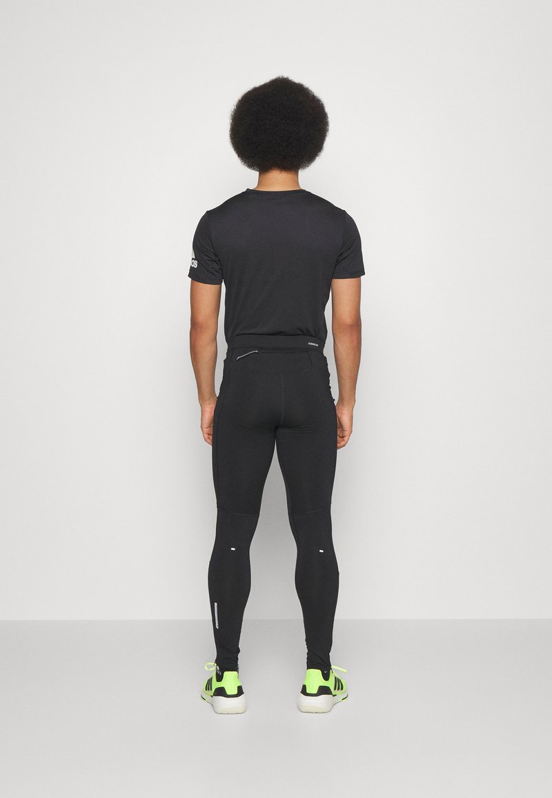 Zwarte atletische T-shirt en strakke leggings met reflecterende accenten. Schoenen zijn felgroen met zwarte details. Gladde, rekbare stof.