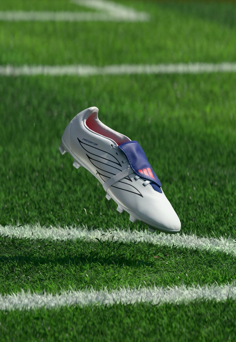 Crampon de football blanc avec languette bleue et rayures noires flottant au-dessus du terrain de football en herbe près de la ligne blanche.