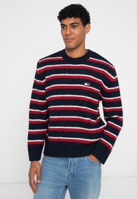 Suéter navy con franjas rojas y blancas, cuello redondo, tejido de punto texturizado, puños y dobladillo acanalados, con un pequeño logo en el pecho.