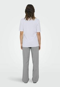 Biała koszulka z krótkim rękawem zestawiona z jasnoszarymi, szerokimi spodniami; prosty design o gładkiej fakturze, minimalne detale widoczne.