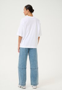 T-shirt blanche surdimensionnée en coton, associée à un jean en denim bleu clair à jambes larges. Texture lisse, design simple sans logos visibles.