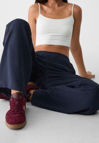 Námornické modré tepláky s volným střihem a elastickým pasem, doplněné bílým crop topem a bordovými teniskami se béžovými akcenty.