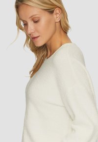 Maglione bianco, con texture, dotato di scollatura rotonda e spalle leggermente scese. Il materiale sembra morbido e accogliente, con una vestibilità rilassata.