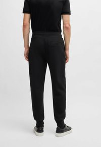 Pantalons de jogging noirs avec une taille élastique, des jambes fuselées et une poche au dos. Le matériau semble doux avec une texture lisse.