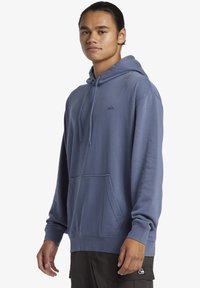 Hooded sweatshirt in light blue, made of soft fabric, features a kangaroo pocket and small logo on the chest. Ribbed cuffs and hem.