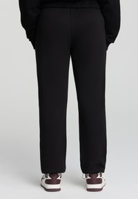 Czarne dresy z elastyczną talią, prostym krojem i ściągaczami. Noszone z białymi oraz bordo sneakersami, widok z tyłu.