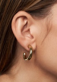 Pendiente de aro de oro con un diseño liso y curvado, sujeto al lóbulo, mostrando una superficie brillante y reflectante.
