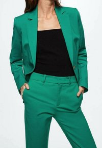 Blazer vert et pantalon assorti en tissu lisse et ajusté. Présente une coupe cintrée, des revers crantés et des poches latérales.