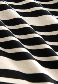 Tejido de algodón con un patrón de rayas onduladas en colores negro y crema alternos, que presenta una superficie lisa y texturada.