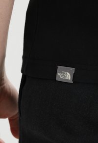 Černé tričko s malou nášivkou s logem "The North Face" umístěnou na spodním lemu, vyrobené z hladké bavlněné směsi.