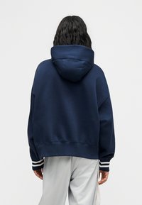 Μπλε ναυτικό φαρδύ φούτερ με κουκούλα και κορδόνι, με ριγέ μανσέτες σε λευκό. Απαλό, υφασμάτινο με υφή, απλός σχεδιασμός.