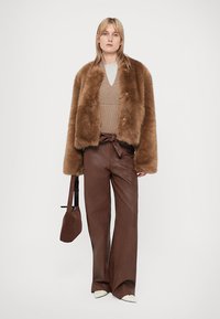 Καφέ ψεύτικο γούνινο παλτό, μπεζ πλεκτή ζακέτα, καφέ δερμάτινο παντελόνι ψηλόμεσο και μια μικρή τσάντα. Τα λευκά τακούνια ολοκληρώνουν την εμφάνιση.