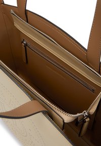 Barna és bézs bőrből készült táska, nyitott főrekesszel, cipzáras belső zsebbel és bézs cérnával díszített külső elülső panellel.