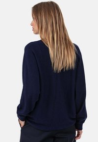Pull marine à coupe décontractée, manches longues et maille texturée. Présente une couture centrale au dos et des poignets côtelés.