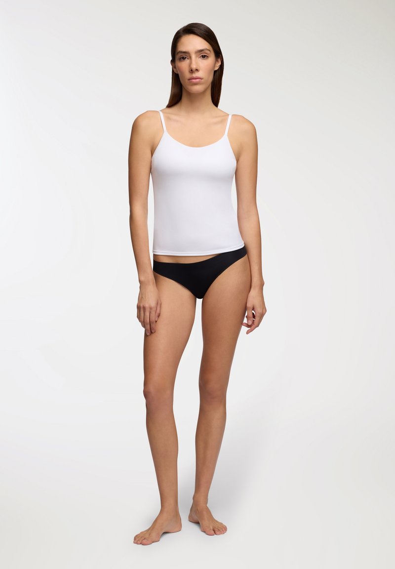 Top bianco senza maniche con spalline sottili e una texture liscia, abbinato a slip bikini neri a vita bassa. Nessun motivo o decorazione notata.