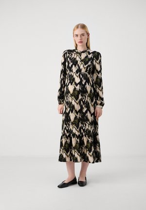 Robe maxi à manches longues en noir, crème et vert avec un motif abstrait. Dotée d'un col rond et d'une taille froncée, elle est associée à des ballerines noires.