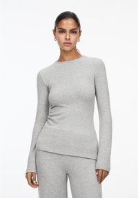 Maglia grigia chiaro a maniche lunghe realizzata in tessuto morbido. Presenta un collo rotondo e un design aderente, abbinata a pantaloni grigi coordinati.
