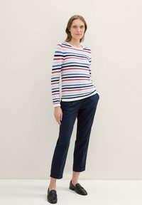 Streifen-Langarmoberteil in Creme, Marineblau, Rot und Blau; kombiniert mit maßgeschneiderten Marineblau-Hosen und schwarzen Slippern; glatte Textur und lässige Passform.
