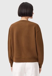 Καφέ, υπερμεγέθη φούτερ με στρογγυλή λαιμόκοψη και χαμηλωμένους ώμους. Μαλακή υφή, με ριμπ μανσέτες και τελείωμα, φορεμένο με λευκό παντελόνι.