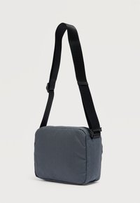 Γκρι τσαντάκι ώμου με καπιτονέ, ορθογώνιο σχήμα, με μαύρο ρυθμιζόμενο ιμάντα και κλείσιμο με φερμουάρ. Υφή με γεωμετρικό σχέδιο.