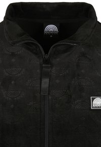 Svart zip-up jacka av mjuk fleece med ett präglat mönster. Har en hög krage och en liten logotyp på vänster sida.