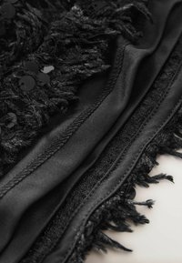 Textil negru cu un amestec de țesătură netedă și textură pufoasă, cu franjuri. Decorat cu paiete negre strălucitoare de-a lungul marginii.