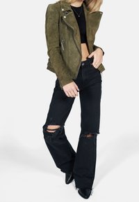 Olive green suede biker jacket with a fitted design and silver zippers, paired with distressed black wide-leg jeans featuring large knee cutouts.