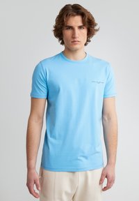 Gaiši zils īsām piedurknēm t-krekls, kas izgatavots no kokvilnas. Tam ir apaļa kakla izgriezums un neliels drukāts logo kreisajā krūšu pusē.