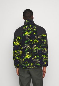Giacca in pile con un vivace motivo astratto verde e nero, colletto alto e tessuto scuro a contrasto sulle spalle.