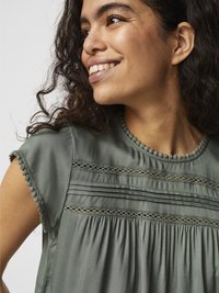 Blouse verte à manches courtes, avec des détails en dentelle texturée et un tissu froncé. Matière lisse et légère avec une coupe décontractée.