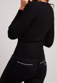 Czarna prążkowana bluzka z długim rękawem i okrągłym dekoltem, z różowym akcentem. W zestawie czarne spodnie z kieszeniami z tyłu zapinanymi na zamek oraz trójkątnym logo.
