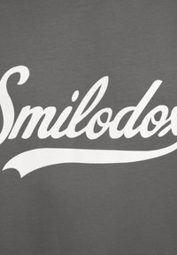 Grå stof med stor, hvid, kursiv tekst, der står "Smilodox" med flydende linjer og en glat tekstur.