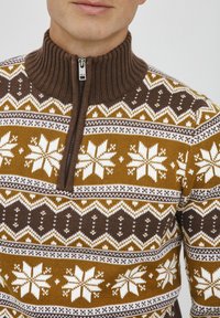 Brązowy sweter na zamek z wysokim prążkowanym kołnierzem. Zawiera dekoracyjny wzór śnieżynek i kształtów geometrycznych w białym i musztardowym kolorze.