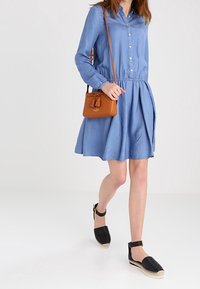 Sininen chambray-paitamekko, jossa pitkät hihat, vyötärö kapeana ja levenevä helma. Yhdistetty mustiin espadrillos-kenkiin ja pieneen ruskeaan olkalaukkuun.