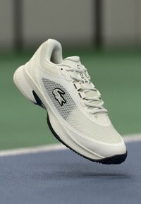 Hvit sportsko med mesh-overdel, gummisåle og svart merkevare. Har rund tå, snøring og teksturerte detaljer.