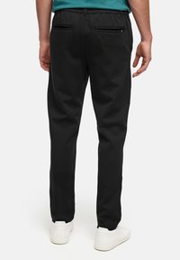 Pantaloni neri con cintura elastica, due tasche posteriori e design a gamba dritta, abbinati a sneakers bianche e una maglietta color teal.