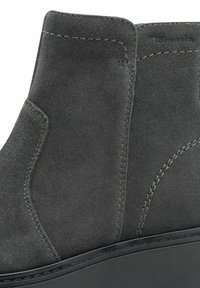 Harmaa mokkanahkainen nilkkuri, jossa on sileä pinta, kaareva muotoilu ja kontrastina musta pohja. Sisältää näkyvät ompeleet ja kulmikkaat sivupaneelit.