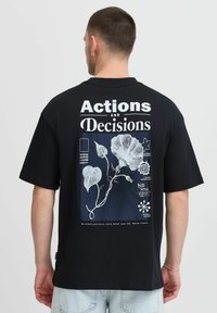 Zwarte katoenen t-shirt met een grafische print op de achterkant, voorzien van witte tekst en bloemillustraties in contrasterende kleuren.